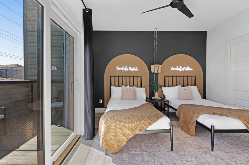 Charming bedroom with two twin beds, a walk-in closet, and a private balcony featuring two chairs for a relaxing outdoor space. The en-suite bathroom includes a sleek shower for added comfort.