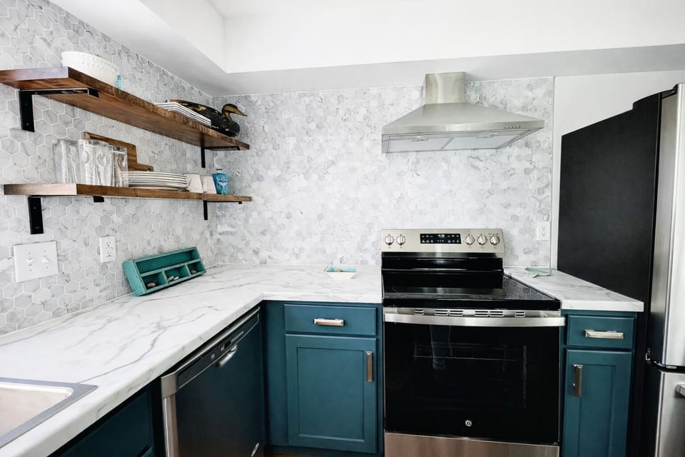 A closer look at the heart of the kitchen reveals a harmonious mix of textures. The marble countertops and geometric backsplash frame the high-quality stainless steel oven, while floating wooden shelves add warmth and practicality.