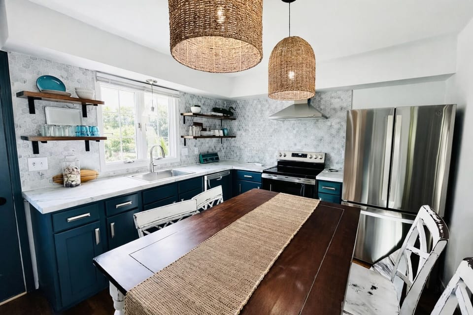 Dine in style under woven pendant lights in this inviting kitchen. The spacious wooden table with rustic accents is perfect for meals or gatherings. The open shelving and farmhouse details create a cozy yet modern ambiance.