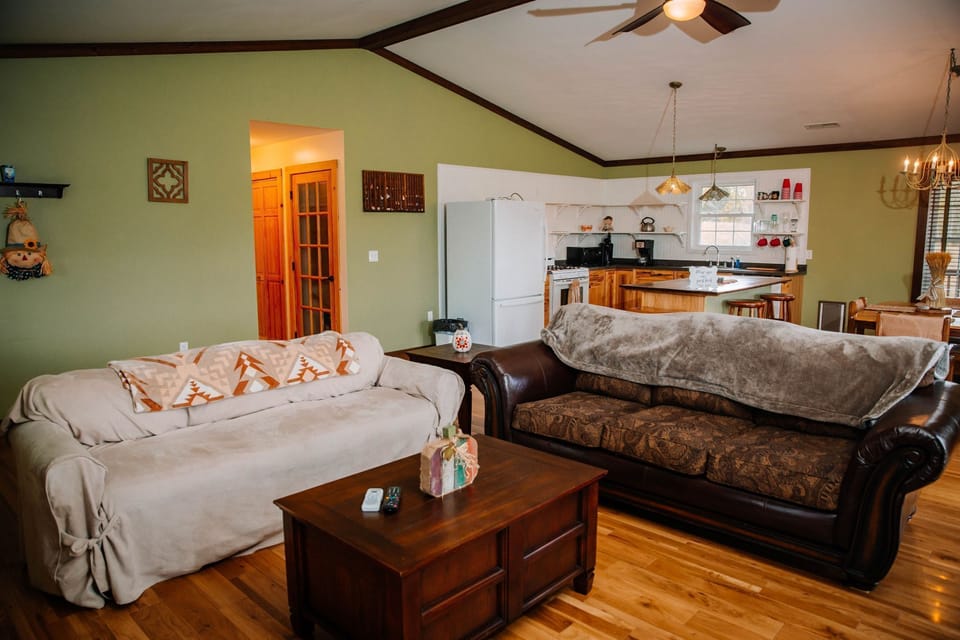 Seamlessly blends the living room with the kitchen, highlighted by soft couches and natural wood finishes for a homely feel.