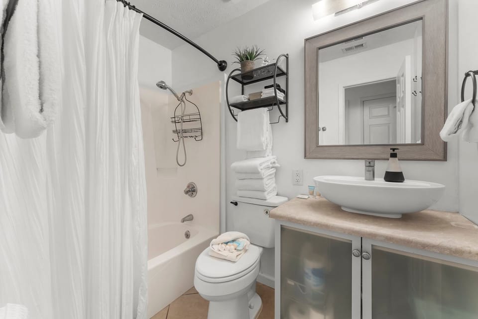 Compact bathroom with a modern vessel sink and shower-tub combination.