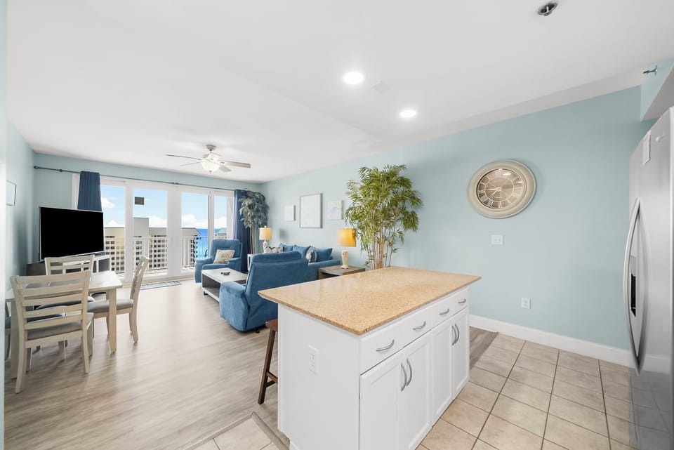 Open-concept living area with coastal blue accents and natural light from balcony doors.