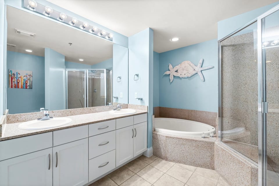 Spacious bathroom with a double vanity and a corner bathtub in a light blue setting.