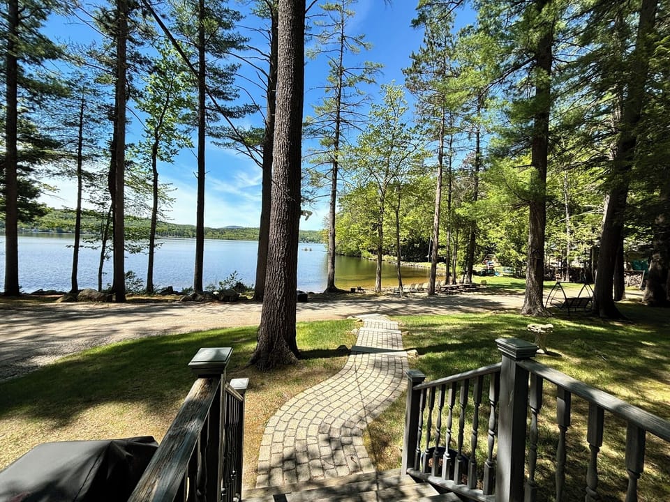 This lakefront rental features a scenic location with a private pathway leading through towering pines directly to the waterfront. The peaceful, tree-shaded grounds provide a serene natural setting for a relaxing getaway.