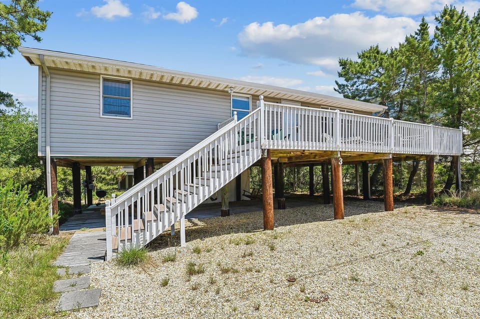 Coastal vacation home elevated on stilts with spacious deck, surrounded by lush greenery and nestled in a peaceful natural setting.