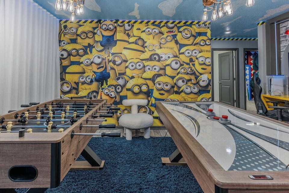 Experience a fun-filled game room for all ages, highlighted by a vibrant Minions mural. Enjoy friendly competition with a sleek foosball table and stylish air hockey setup, all on cozy blue carpeting that adds to the excitement.