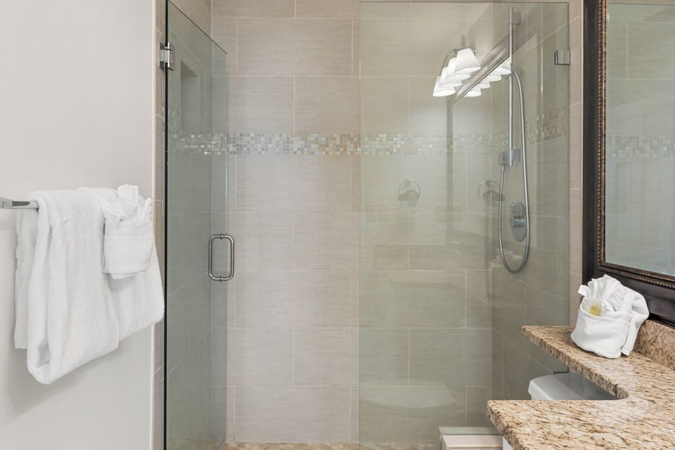 Step into your spa-like bathroom featuring a spacious glass shower with elegant mosaic tile details and plush towels ready for your stay.