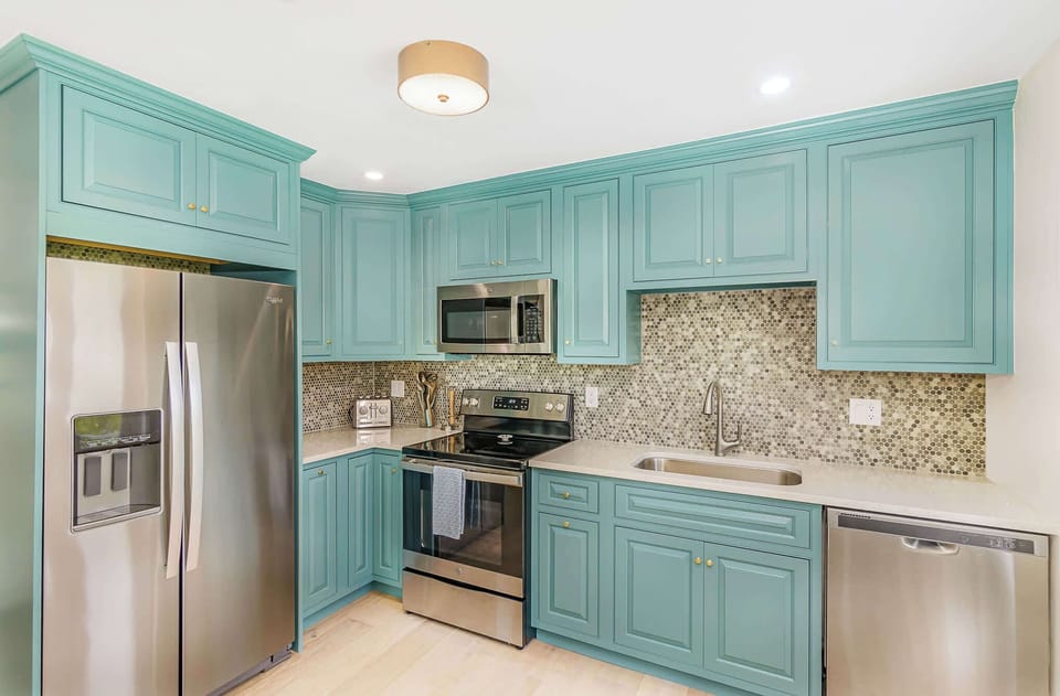 Modern kitchen featuring teal cabinetry and stainless steel appliances with a mosaic tile backsplash.