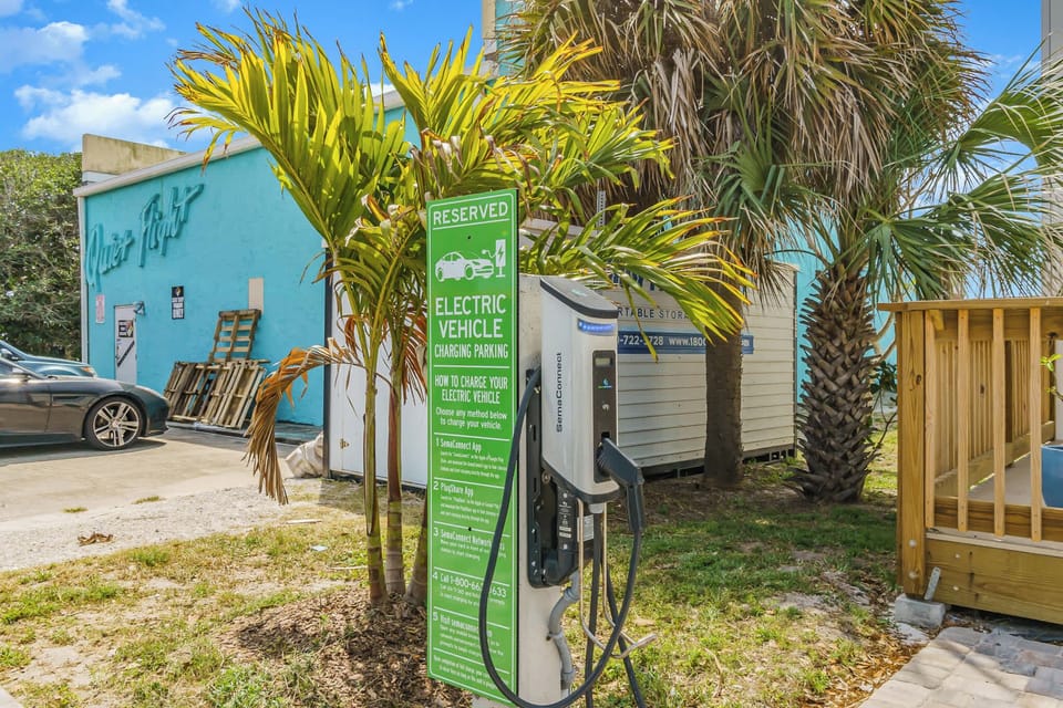 Electric vehicle charging station surrounded by tropical palm trees near a turquoise building.