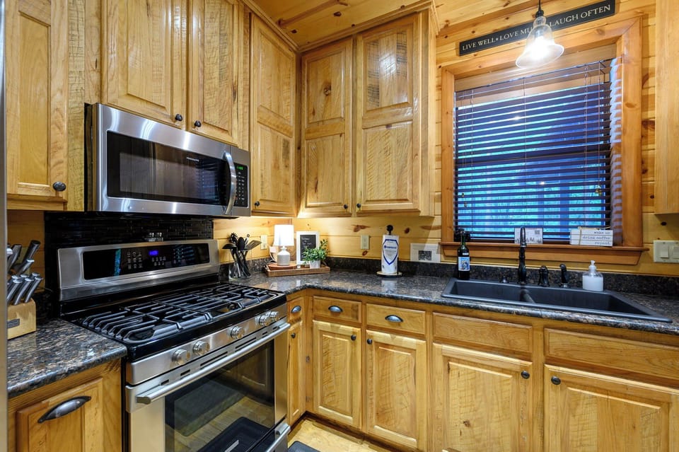 Inviting cabin kitchen featuring warm wood tones, stainless steel appliances, and granite countertops bathed in natural light. Perfect for preparing your favorite meals.