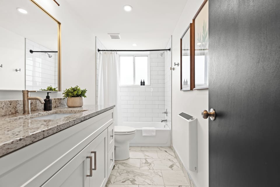 Enjoy a clean and modern bathroom with elegant white tile, granite counters, and a full-size tub and shower combo.
