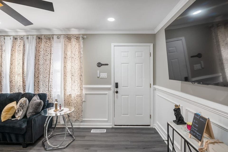 Relax in a cozy and modern space with a comfy sofa, large flat-screen TV, and ceiling fan. Natural light and an open layout flow seamlessly into the kitchen, creating a warm and inviting vibe.