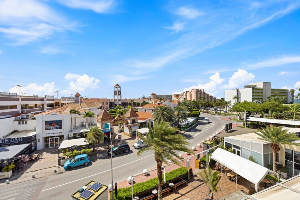Take in this fantastic view from the balcony! You’ll see charming shops, palm trees swaying, and the vibrant atmosphere of the area—perfect for enjoying a sunny day!