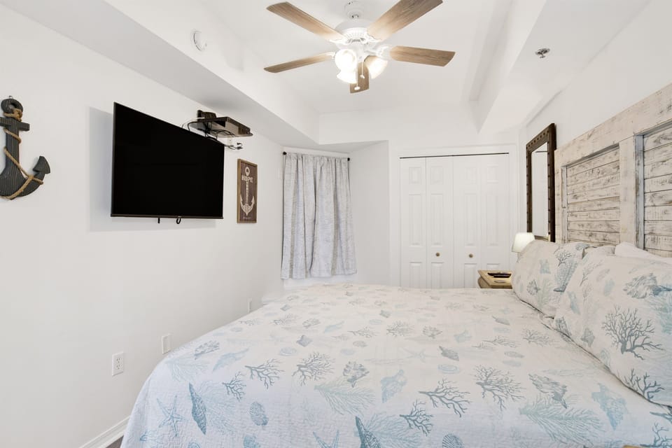 Bedroom with king bed, ceiling fan, 2 nightstands with mirrors wall mounted above, 50" Wall mounted smart tv, double closet, dresser, blackout curtains and ensuite bathroom
