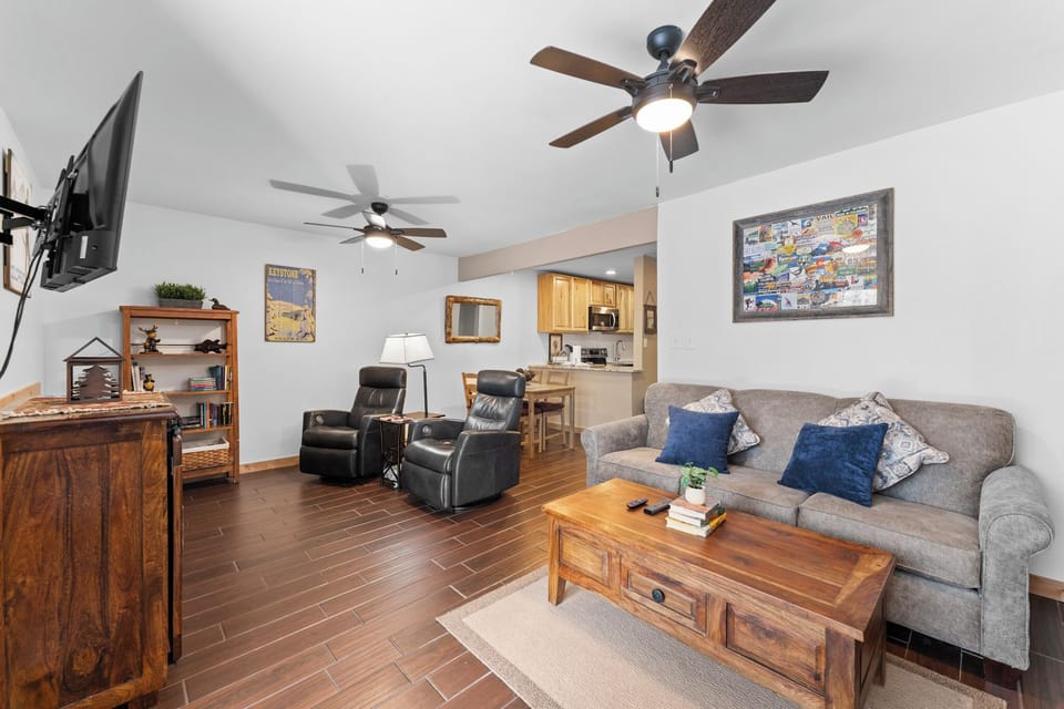 Relax in your spacious living room featuring plush seating, ceiling fans, and warm wood accents that create the perfect atmosphere for unwinding.