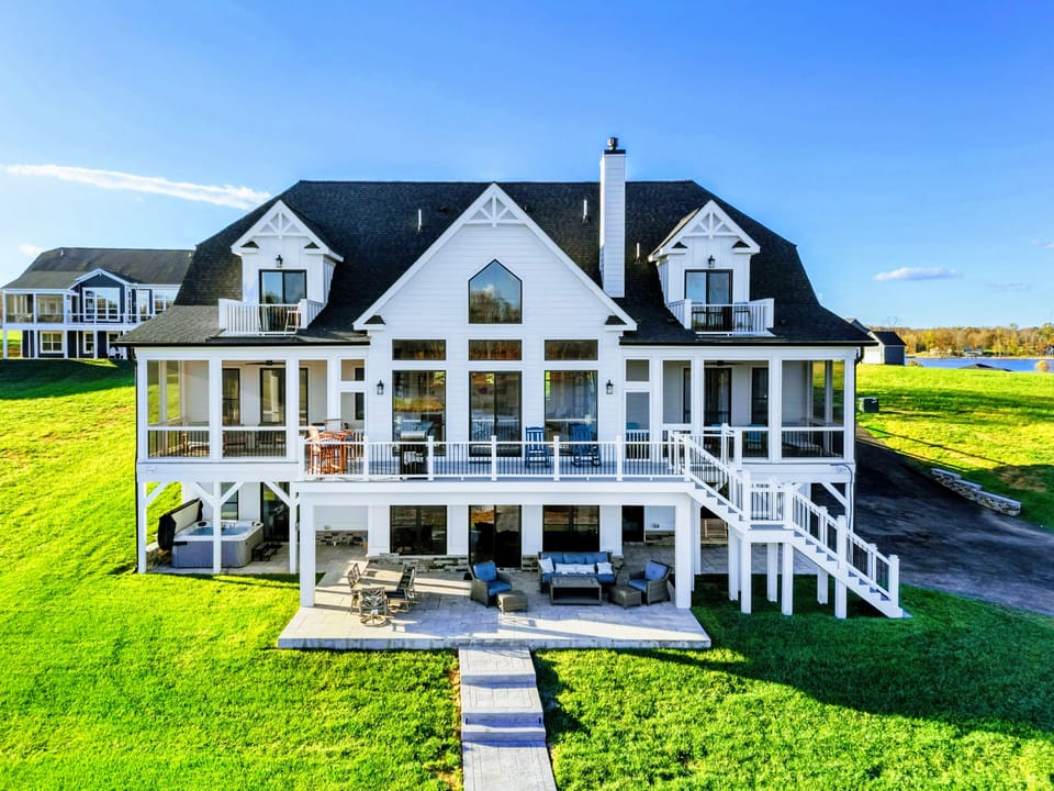 Expansive lakeside home with a modern farmhouse design, multiple balconies, screened porches, and a spacious outdoor patio for relaxation and entertainment.