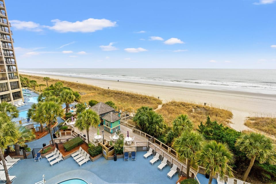 Balcony view overlooking Beach Cove Resort’s tropically themed pools, hot tubs, lazy river, and poolside beach bar, with sweeping views of the North Myrtle Beach shoreline and Atlantic Ocean.