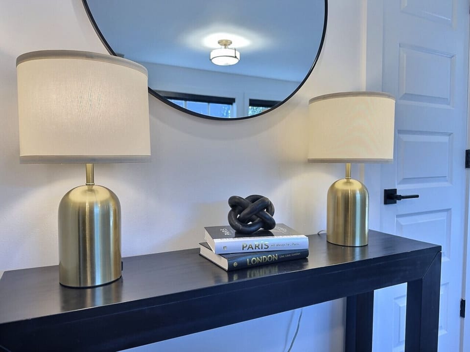 A modern console table accented with brass lamps, decorative books, and a sculptural knot piece for a chic, welcoming look in this furnished apartment.