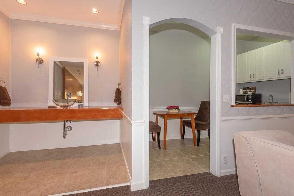 Wall-mounted mirror and glass vessel sink with wooden countertop, adjacent to an arched dining nook with a wood table.