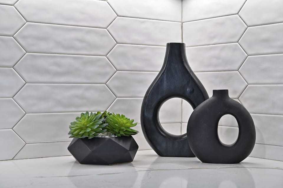 Modern accent corner — featuring matte black sculptural vases and a geometric planter with faux succulents, set against a chic textured tile backdrop.