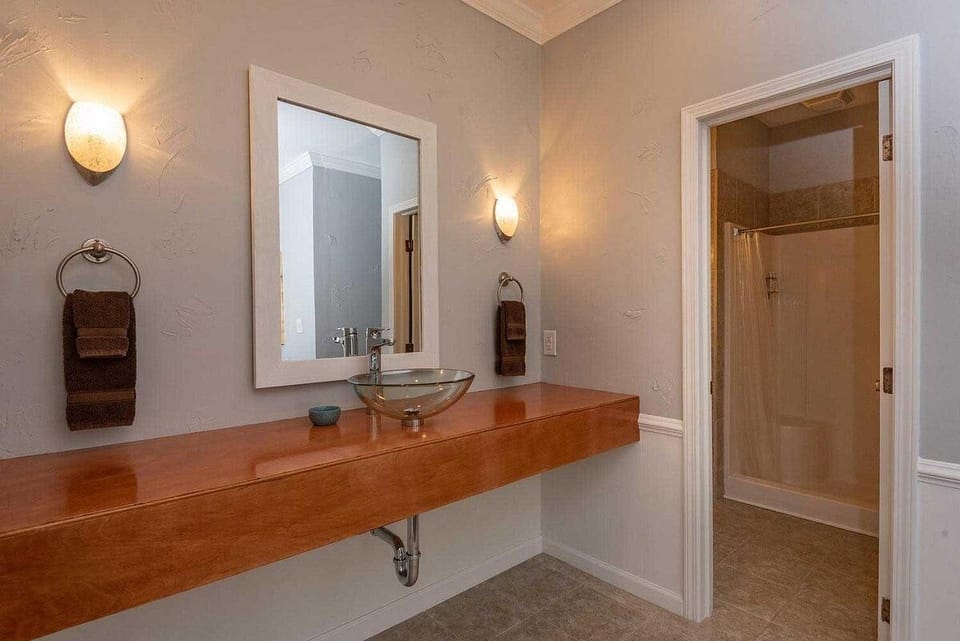 Wall-mounted frosted glass vessel sink rests on a wood floating countertop with matching brown towels.