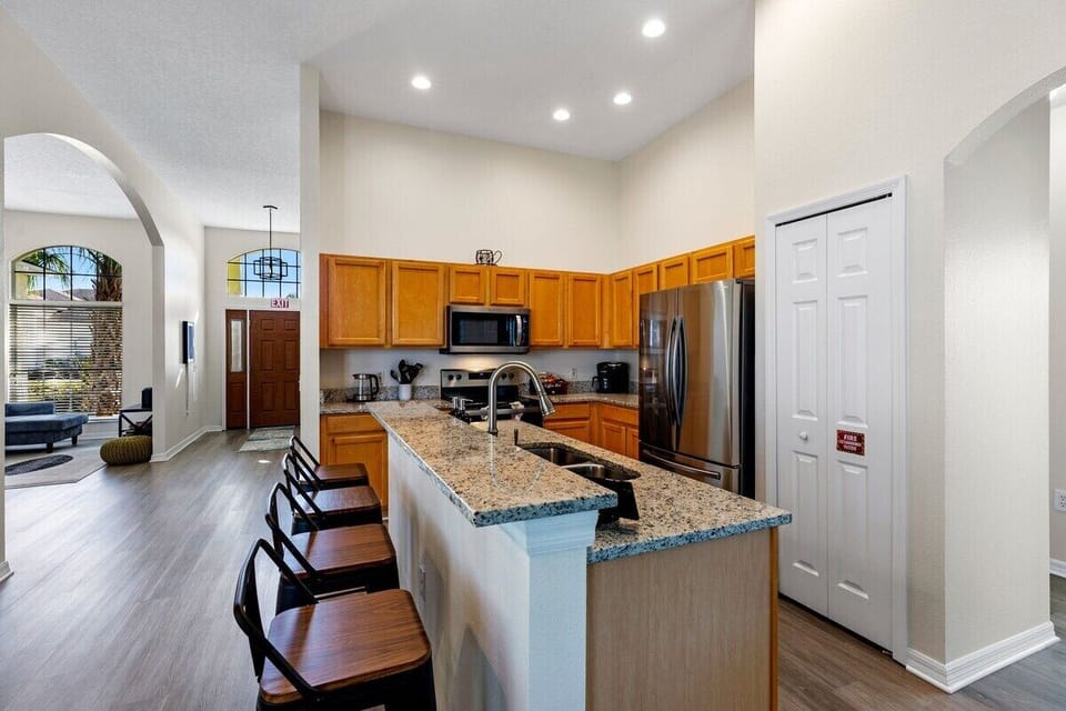 This modern kitchen features stainless steel appliances, a large center island with bar seating, ample counter space, stylish lighting, and an open layout connected to the breakfast nook.