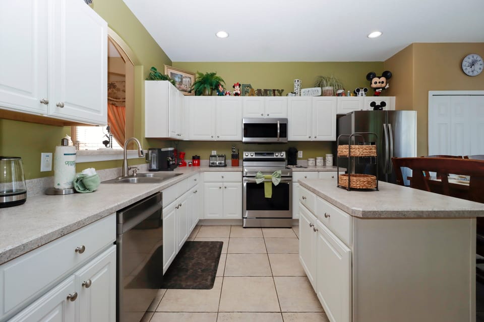 The kitchen features a spacious layout with white cabinetry, a center island for prep space, stainless steel appliances, built-in microwave, and adjoining dining area.