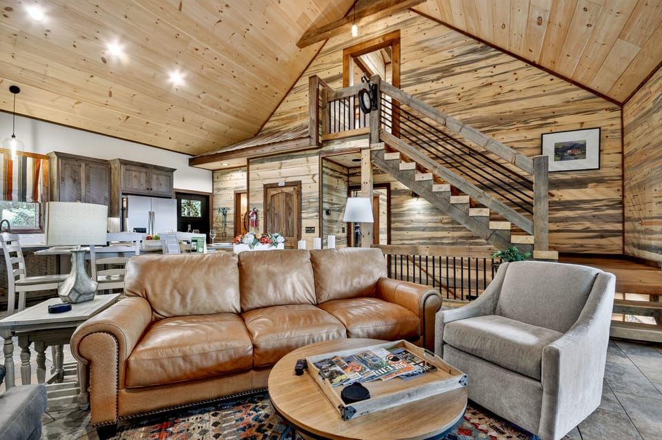 Soaring ceilings, a wall of windows, and a floor-to-ceiling stone fireplace make this stunning living room the heart of this Ellijay cabin rental