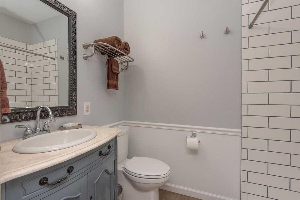 Bathroom with white subway tile shower, marble countertop, vintage-style blue vanity, and brown towels on rack.