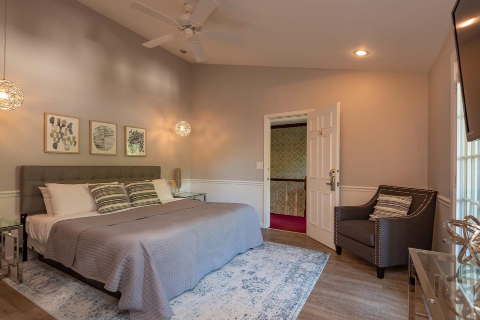 Gray armchair with nailhead trim and striped pillow sits beside a glass console under wall-mounted TV.