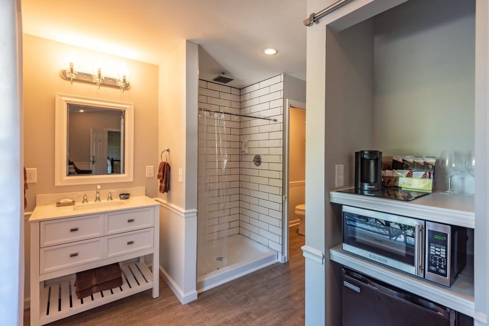 Bathroom vanity with white drawers and silver fixtures sits beside a walk-in shower with subway tile and clear curtain.