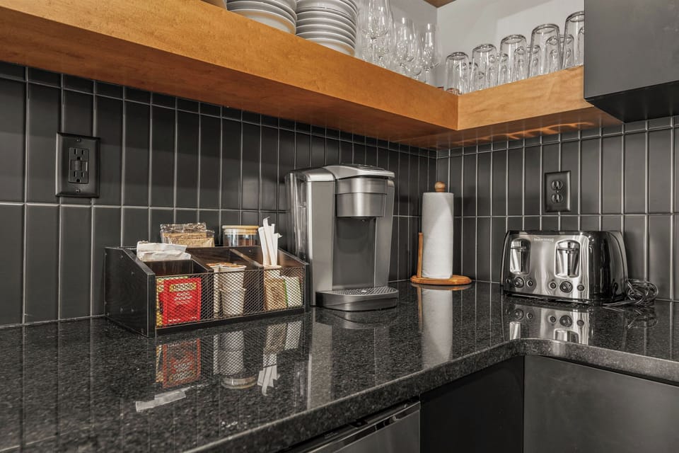 - Start your morning right with a fully stocked coffee and tea bar, complete with a Keurig
- Everything you need, from mugs and sweeteners to stirrers, is within arm's reach
- Sleek black tile backsplash and wood shelving add modern flair