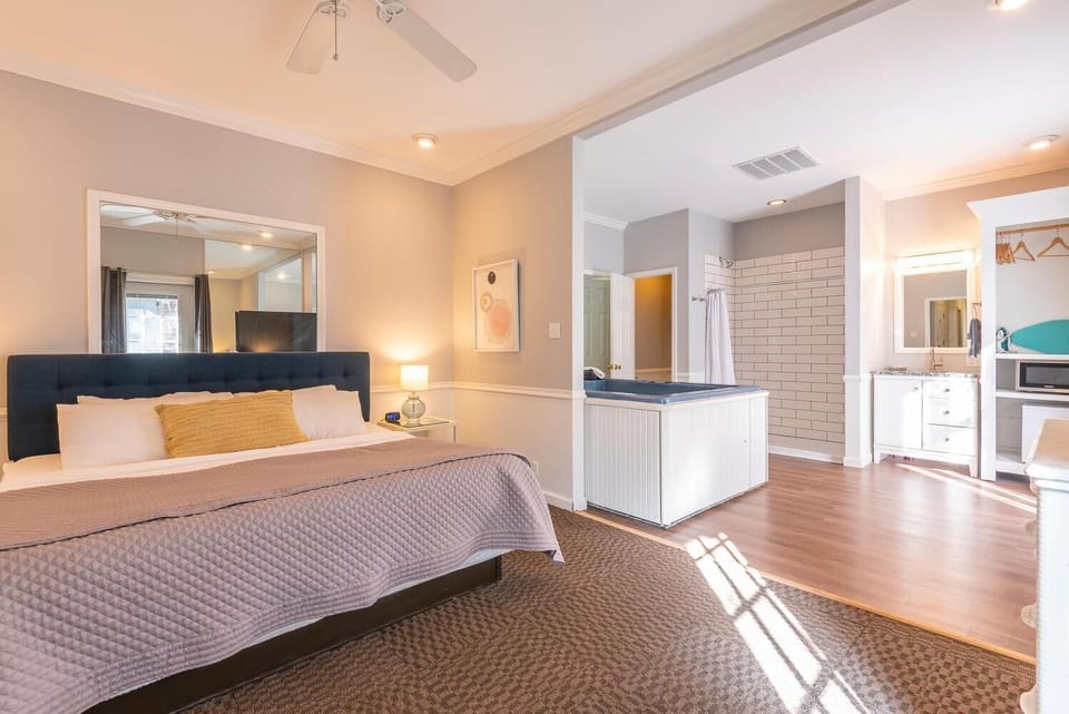 King bed with tufted navy headboard faces a large mirror and soft lighting in the bedroom area.
