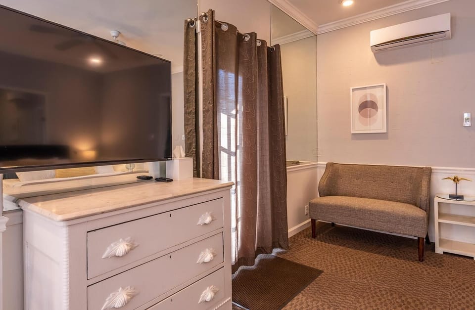 Gray-brown loveseat sits beside a white nightstand with gold bird sculpture under abstract wall art.