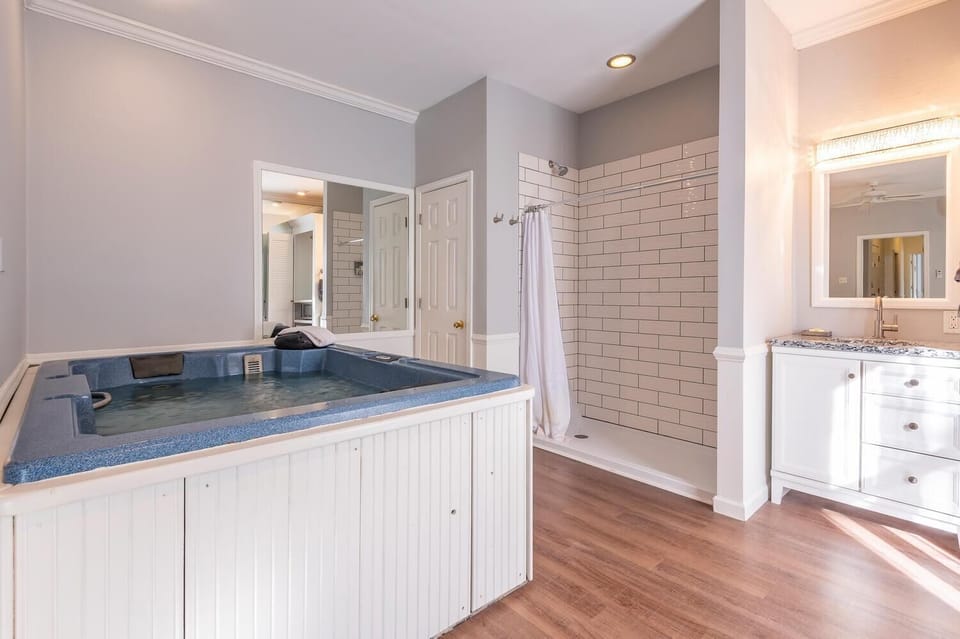 In-room hot tub with blue textured surround beside a white subway-tiled shower and white vanity on wood flooring.
