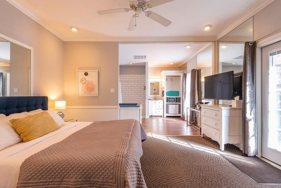 Suite with king bed, navy tufted headboard, white dresser, wall mirror, and glass door leading outside.