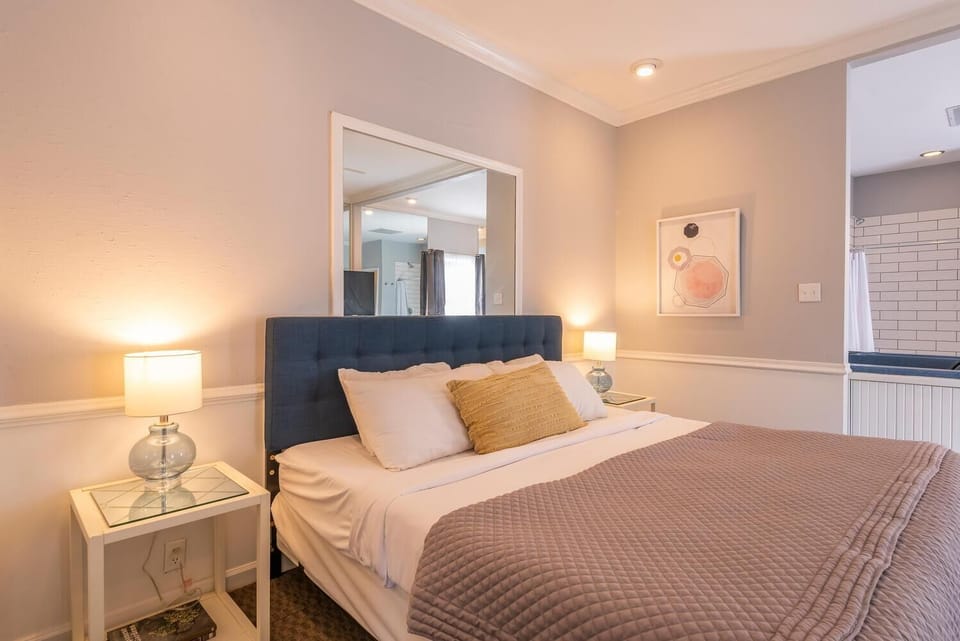 Soft bedside lamps glow on glass-top nightstands beside a king bed with a navy tufted headboard and textured blanket.