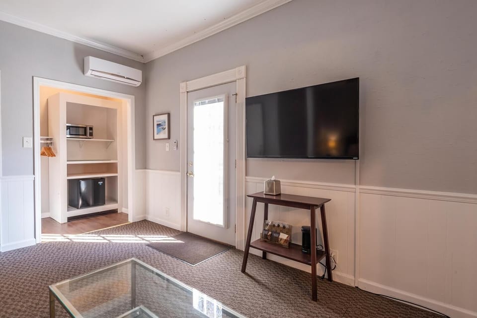 Flat-screen TV mounted above a dark wood console table with coffee supplies next to a door with frosted glass.
