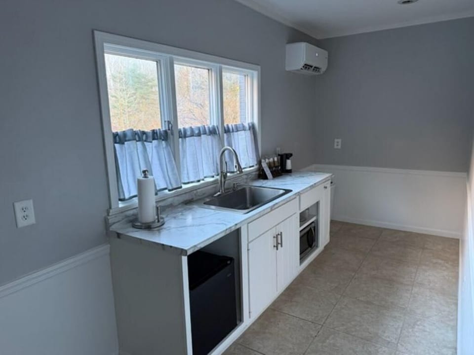 Marble-look countertop stretches beneath a triple window with short gray curtains in compact kitchenette.