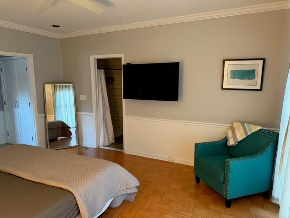 Teal armchair with nailhead trim sits beneath abstract art and next to a wall-mounted flat-screen TV.