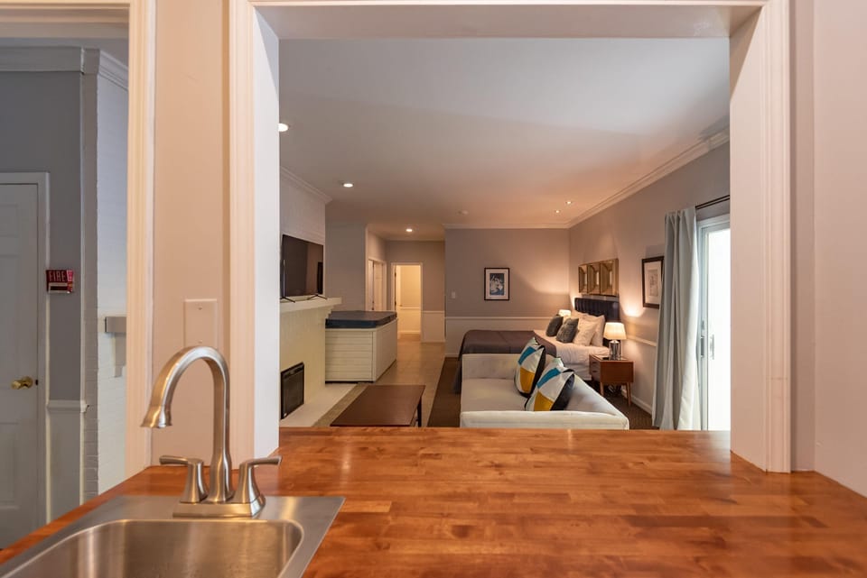 View from the kitchen sink through a pass-through window into the living area with white sofa and king bed.