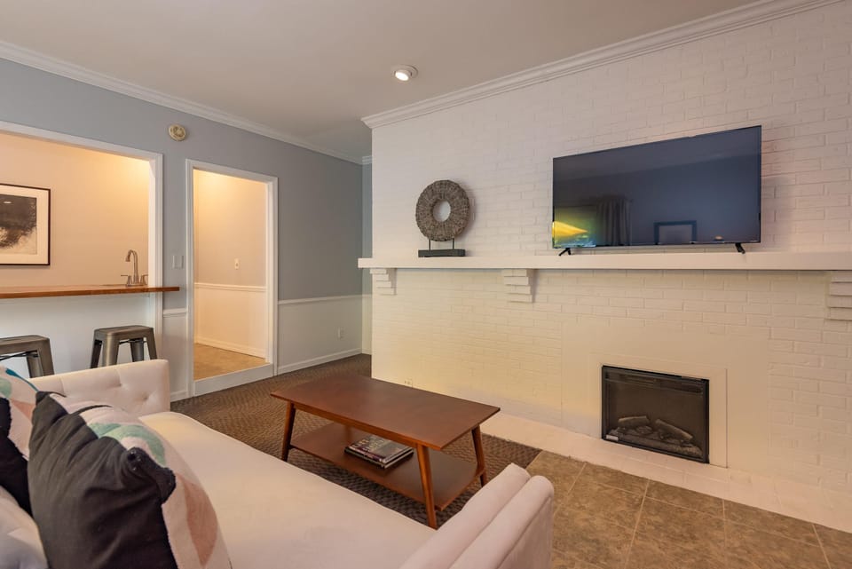 White brick fireplace wall with mounted flat-screen TV, wood coffee table, and tufted white sofa.