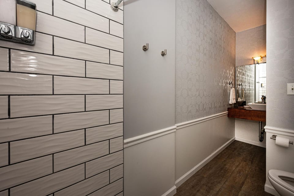 Narrow bathroom hallway with patterned wallpaper, dark wood floor, floating wooden vanity, and wall-mounted mirror.