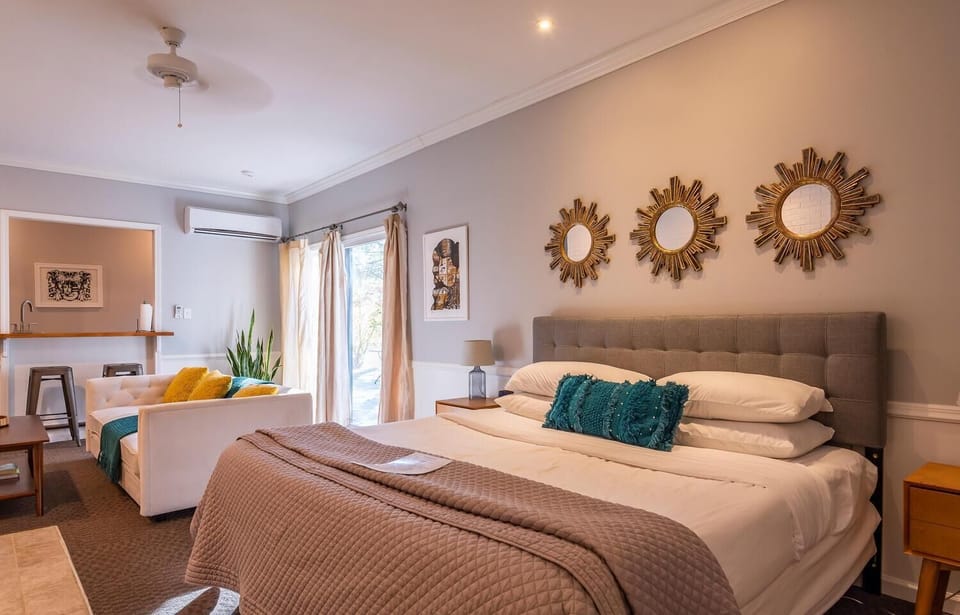 Bedroom features a gray tufted headboard, sunburst mirrors, and teal accent pillows on white bedding.