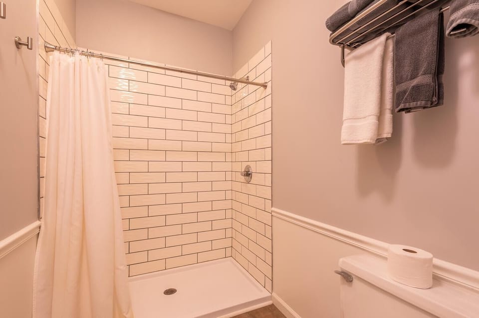 Bathroom shower area with white subway tiles, chrome fixtures, and a white fabric shower curtain.