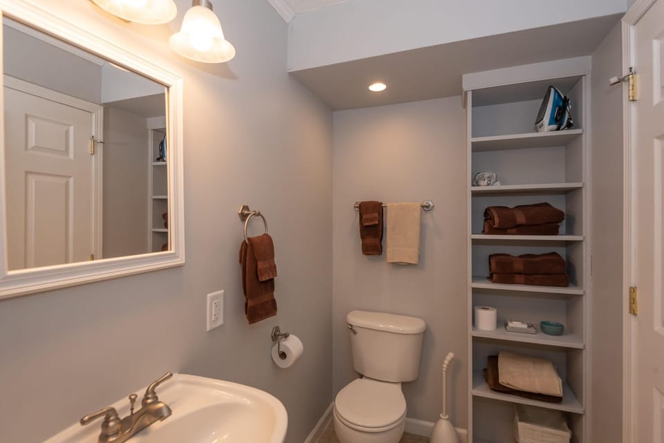 Bathroom with soft gray walls, white trim, open shelving stocked with folded towels, and brushed nickel fixtures.