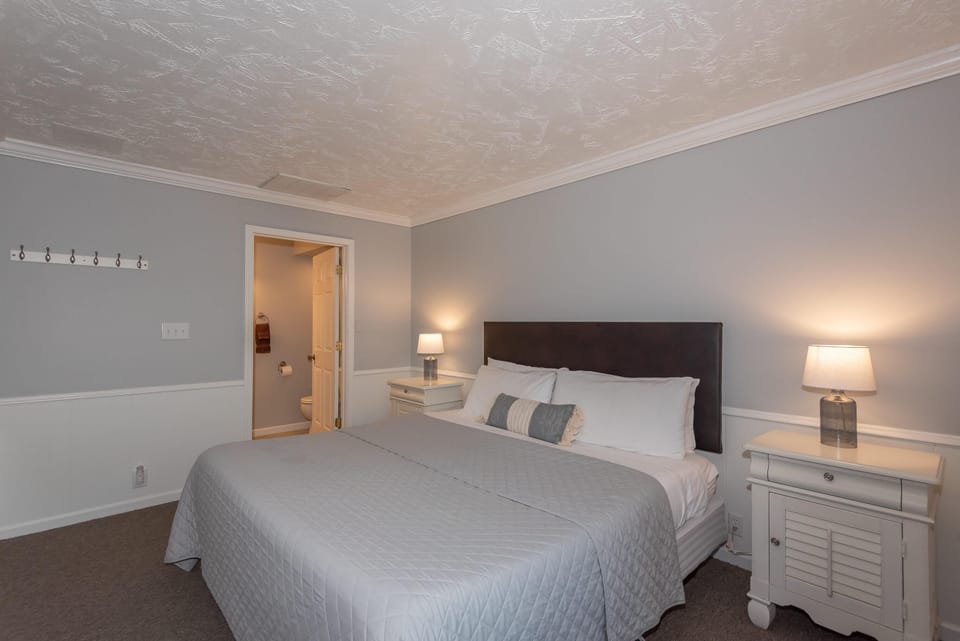 King bed with gray quilt and white linens, flanked by white nightstands and glass table lamps.