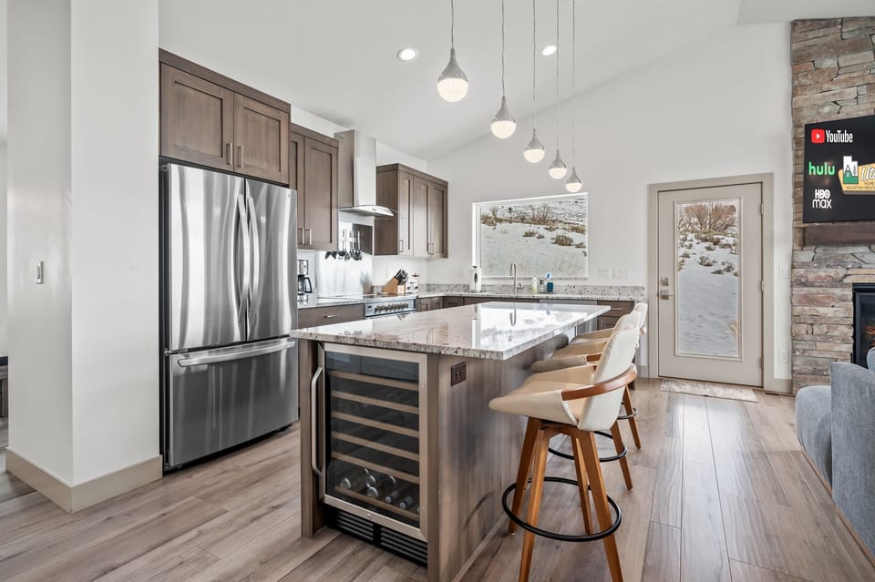 The gourmet kitchen features an island with seating for three and is equipped with stainless steel appliances, including a microwave, electric stove, and spacious refrigerator.