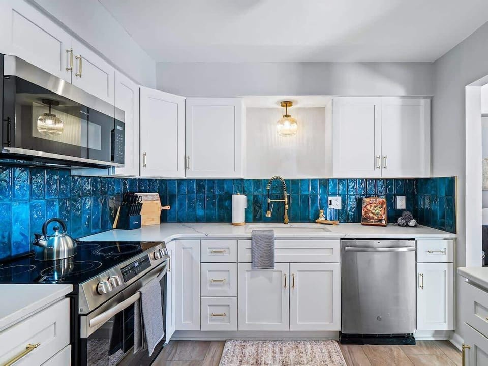 Bright kitchen w/ white cabinetry, stainless steel appliances & vibrant tile backsplash