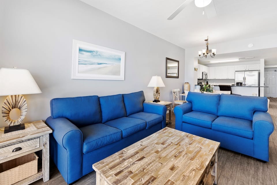 Sink into plush blue sofas in your bright living space, where coastal artwork and open kitchen create the perfect retreat.